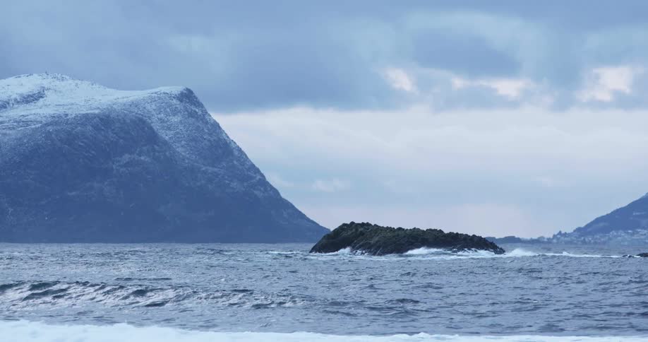 An islet sits off the coast amidst large ocean waves