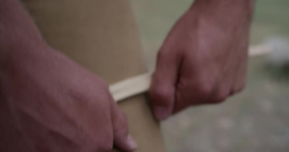 A man is breaking wood over his leg then putting it on a table