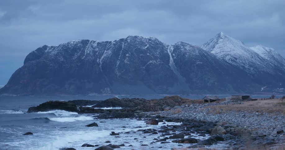 Waves washing into a rocky beach beneath a snow capped mountain