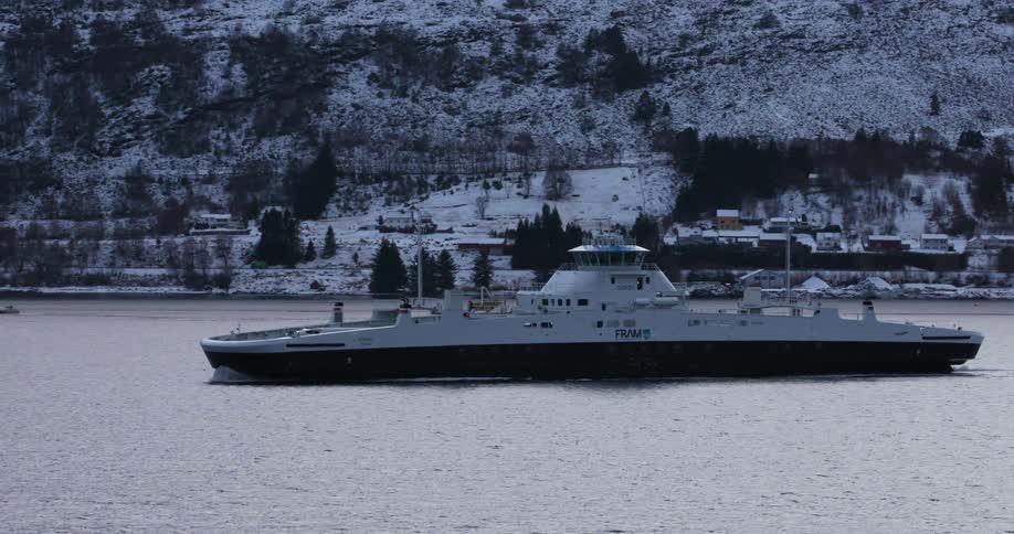A yacht sails by a snow covered mountain where houses sit near the base