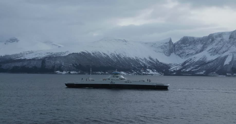 A large ship traveling through the ocean near snow covered mountains