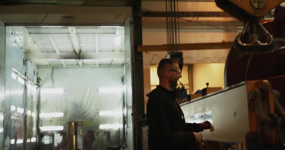 A man holding a controller walks in a factory and reaches up to stop and touch a moving pulley