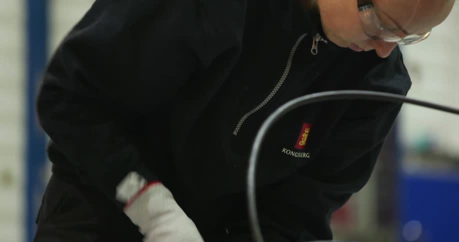 A factory worker uses a tool to tighten a screw on a metal canister