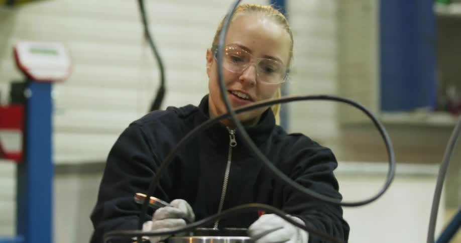 A woman smiles as she turns a lever on a canister in a factory