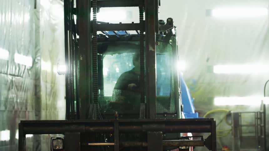 A man drives a forklift inside of a building covered in plastic wrap