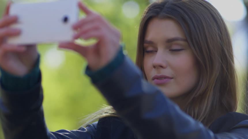 Woman stands and takes a selfie with her smartphone