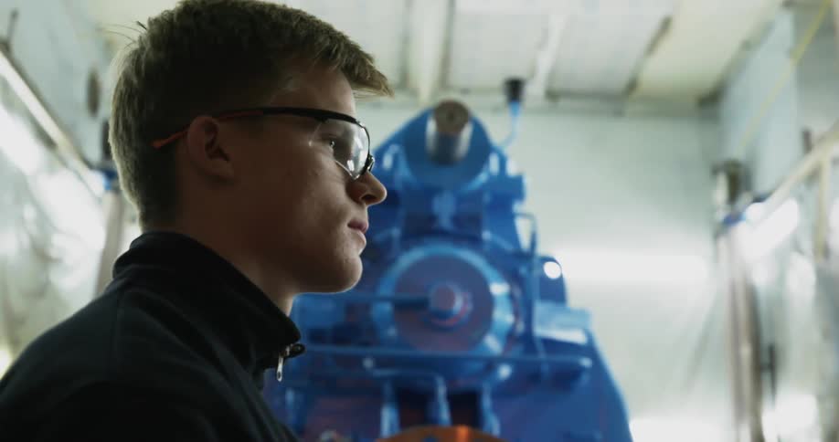 Young man wearing protective glasses stand near big engine