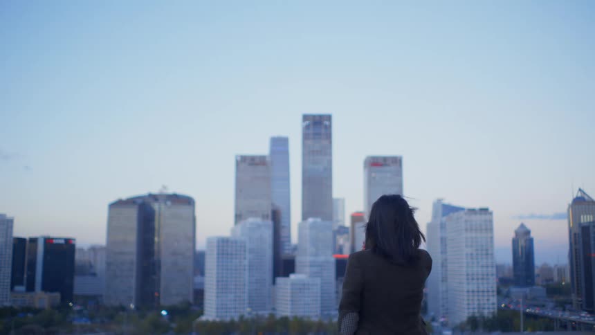 A woman holds her cell phone and takes a photo of the downtown Beijing skyline