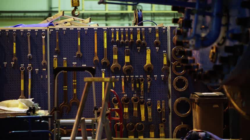 A row of hand tools hanging in a factory as a worker works on a machine