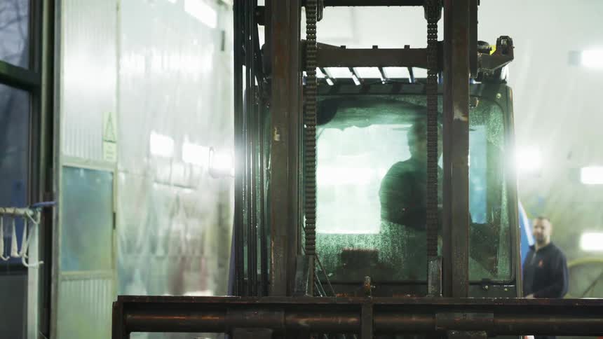 A worker backs up a forklift as a coworker looks on
