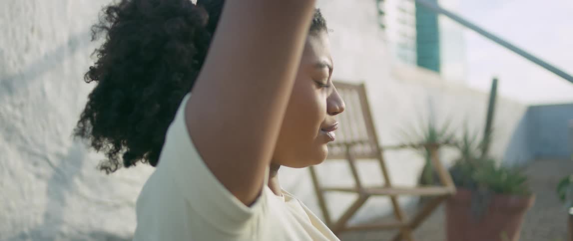 A black woman sits on a balcony in a city and practices yoga