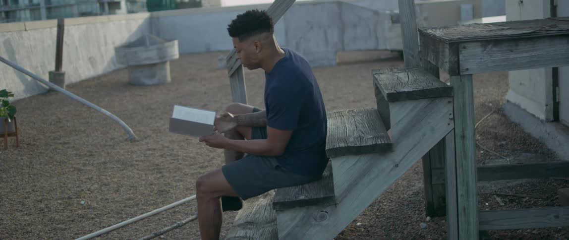 A teenage boy sits on rooftop steps reading a book
