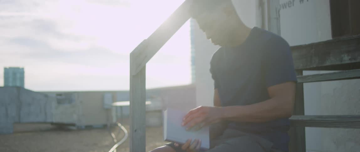 A man carrying a book walks over to the steps and sits down to read in the sunshine