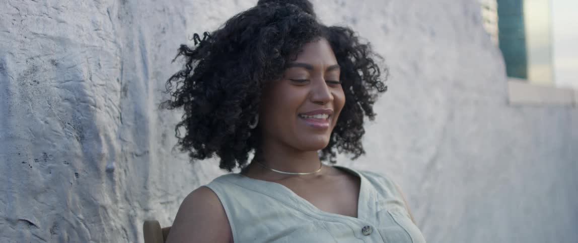 A woman smiles and closes her eyes as she poses next to a wall on a building rooftop