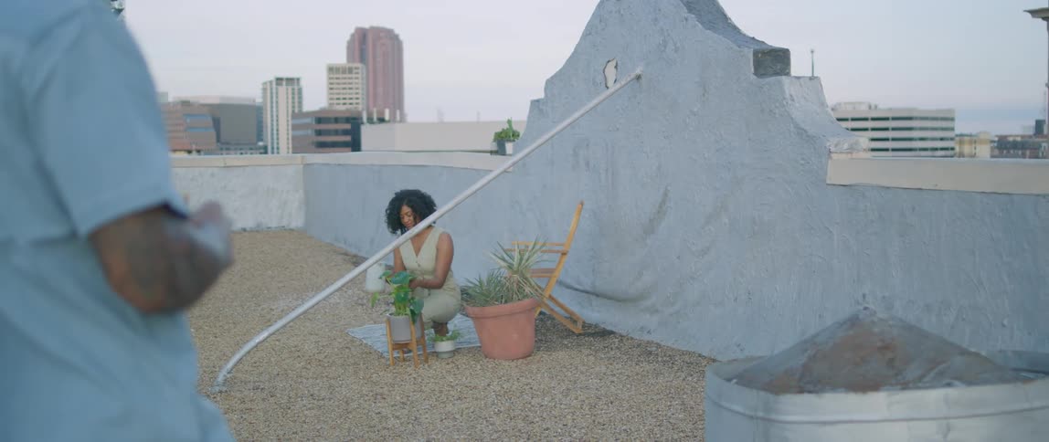 A man stands on a rooftop as a woman water plants