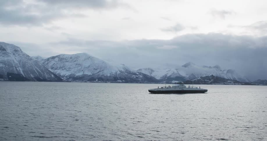 Ship travels across the sea with the snow capped mountains in the background