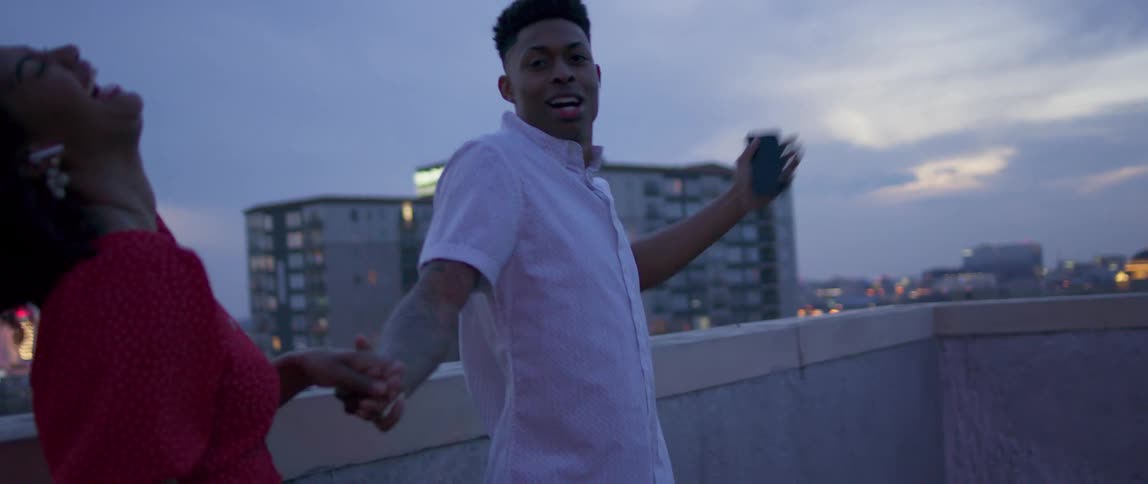 Two black people dance and laugh on a rooftop in the city