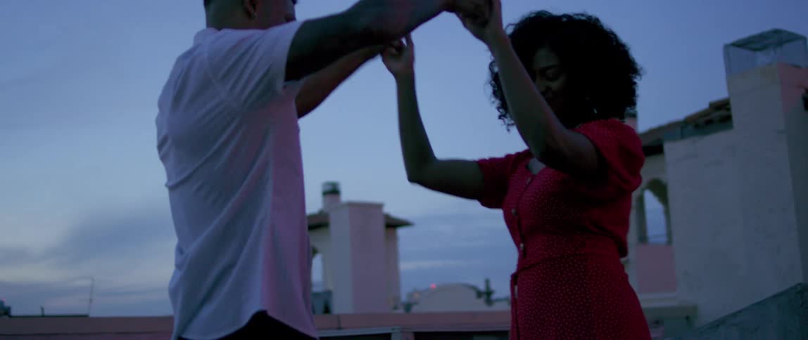 A man and woman dance on a roof top in a neighborhood