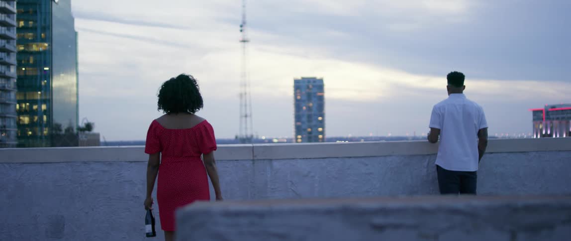 A woman with a bottle of wine walks up to a black man
