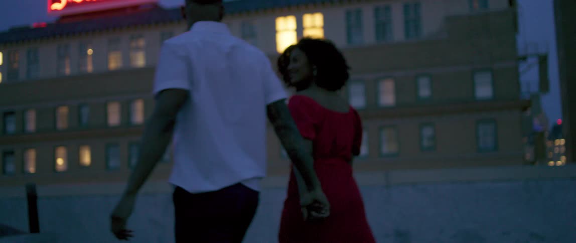 Couple dancing on the roof top next to lighted apartment signage
