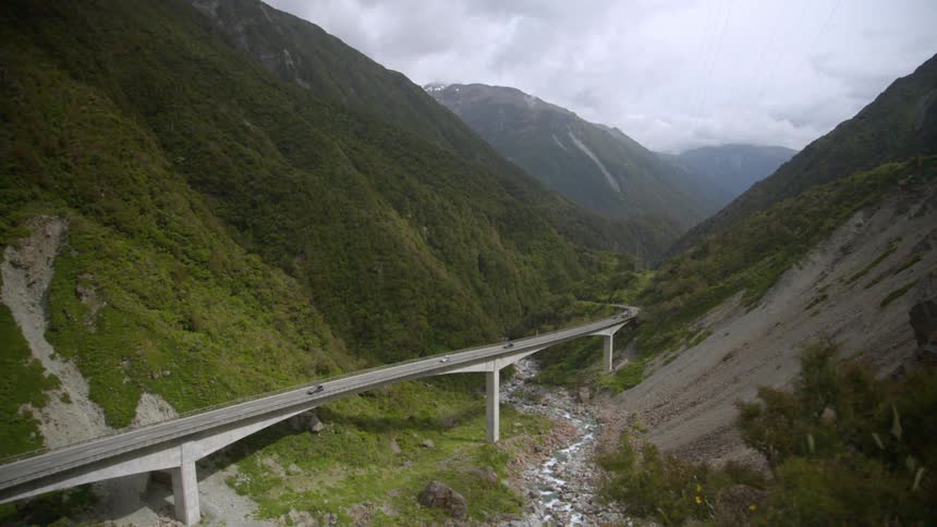 Cars travel on an highway bridge over a ravine between hill slopes