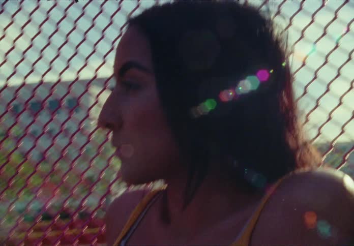 Woman sitting on the wall in front of the wire fence looks around on a sunny day