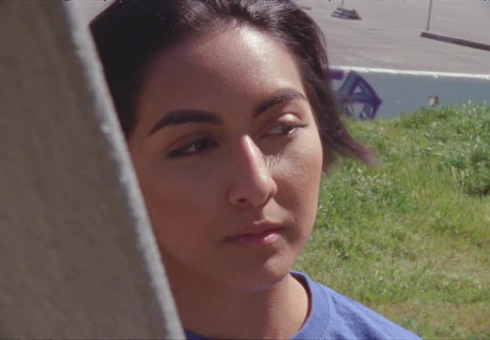 A hispanic teenager stands outdoors during the day and looks about