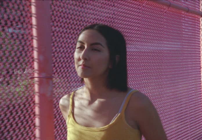A hispanic teenager walks along next to a fence
