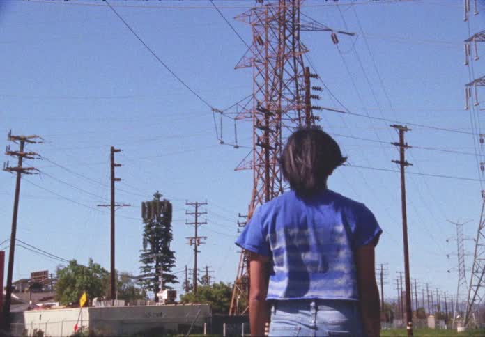 A young woman walks near buildings and transmission towers