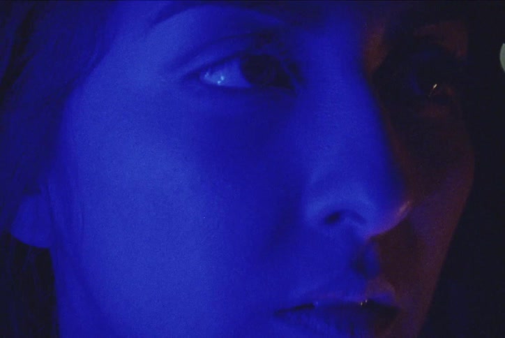 A young woman looks straight ahead as a light flashes in the distance