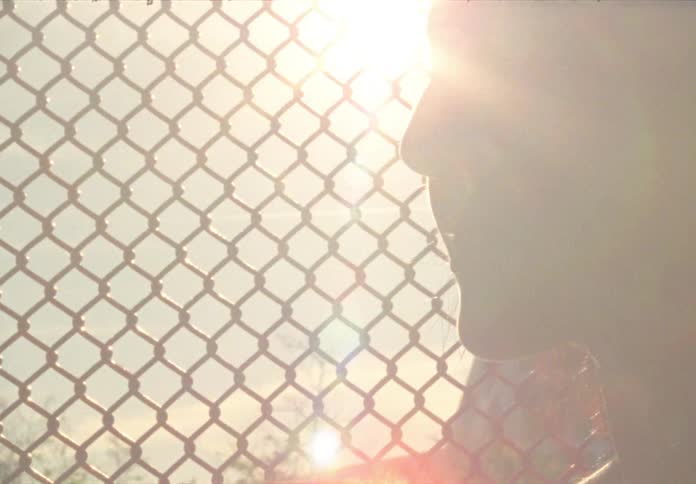A woman purses her lips as she stands outside next to a chain link fence