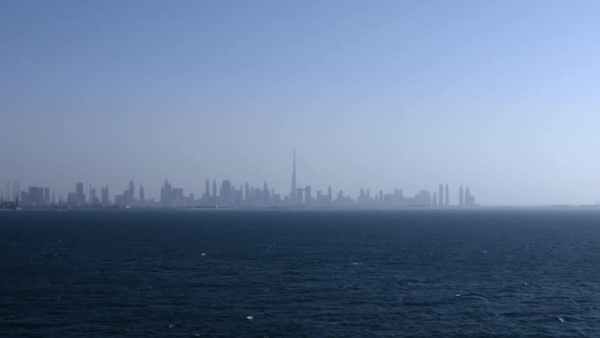A city skyline is silhouetted behind the ocean