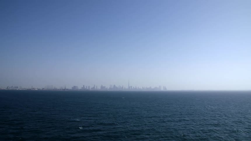 The vast and calm ocean under the blue sky with skyscrapers visible far in the distance