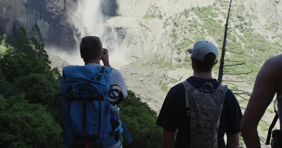 Men standing on a mountain cliff as one photographs a waterfall