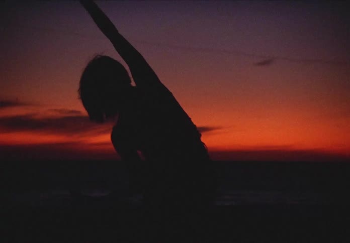 A silhouette of a woman dances on the beach at sunset