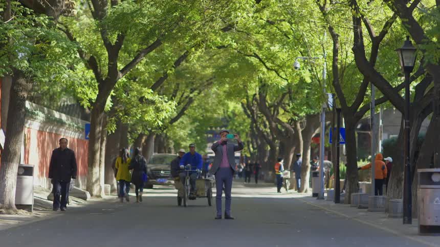 A white man standing in a street in asia talking photographs with his blue smartphone