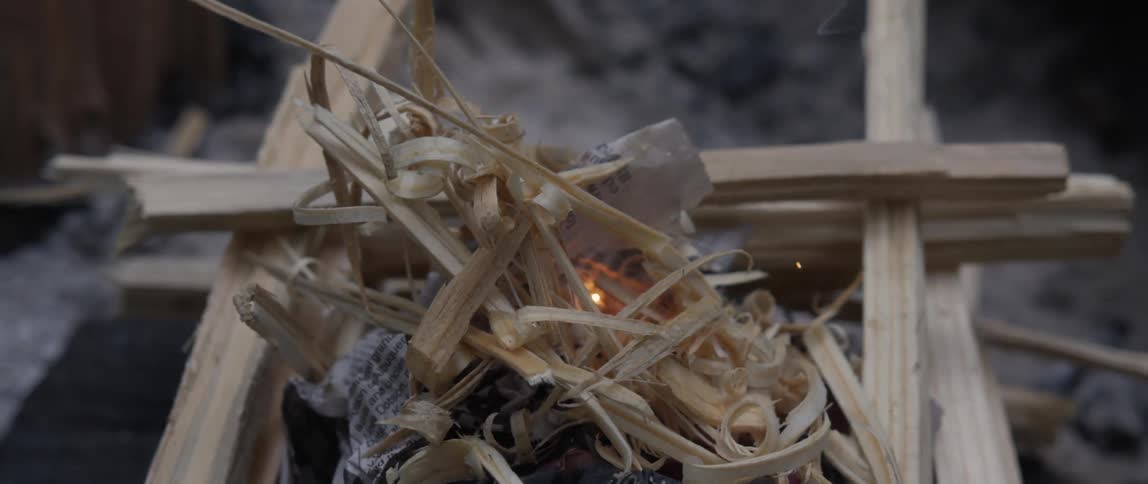 Sparks fly toward kindling and paper stacked to create a fire