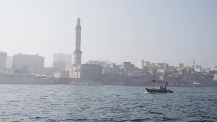 Small boat travels across the sea with the city skyline in the background