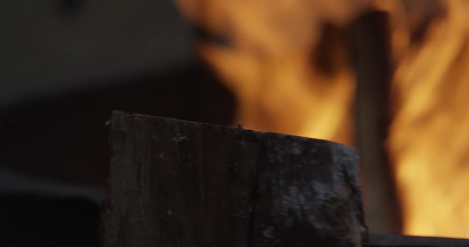 A beer bottle being opened on a log with a campfire burning in the background
