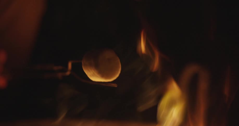A person is cooking marshmallows on a fire at night