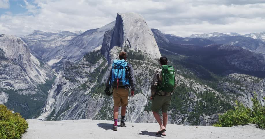 Two men walk up to a ledge and take pictures of a mountain