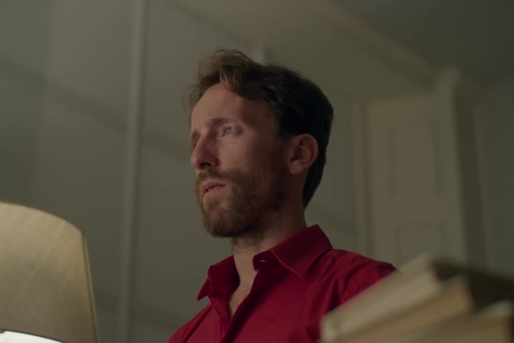 A white man sits in a room listening to a smartphone