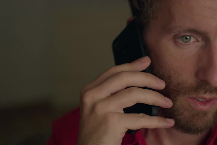 Male holding a cell phone up to his ear swallows while listening with a concerned look on his face before he starts to speak