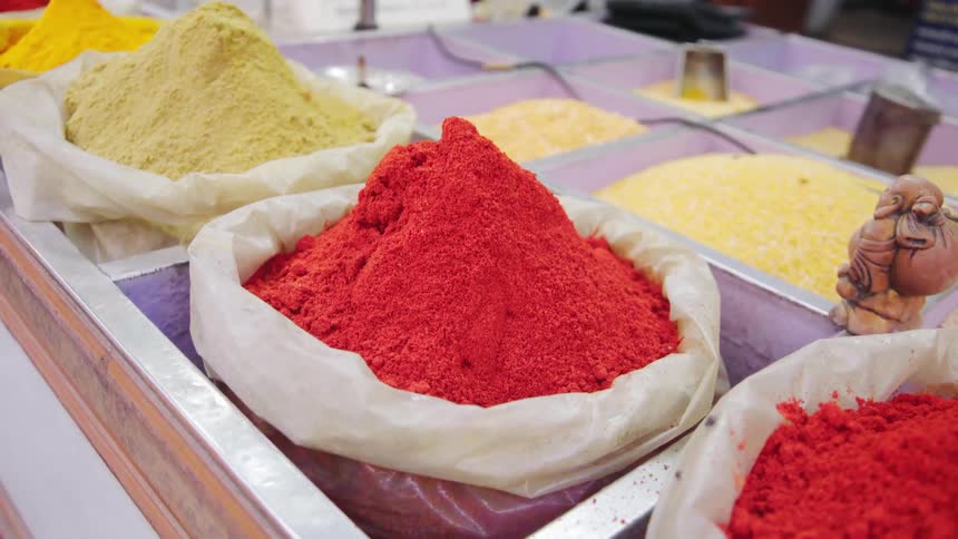 Flies buzz around bins full of spices at a market