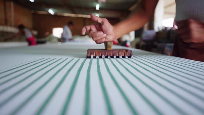 A man uses a wooden tool to hand stamp dye onto fabric in a striped pattern