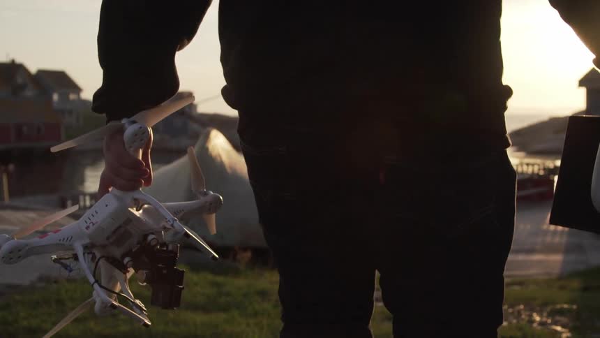 A man carrying a drone walks towards the shore