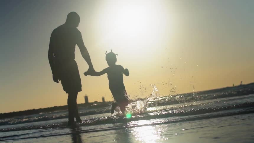 A father and daughter splash around in the tide at the beach