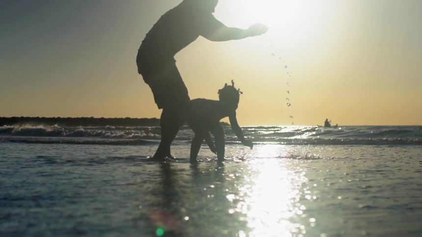A black man and his daughter splash in the tide on the beach