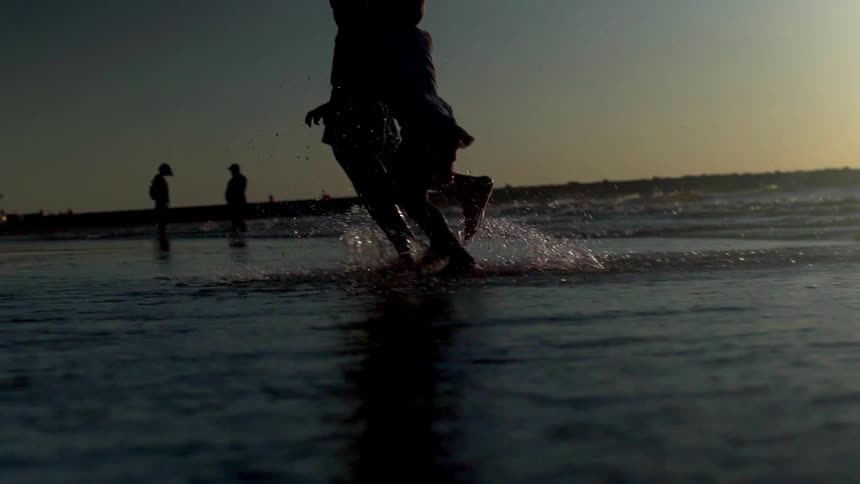 A silhouette of a father and daughter run on the beach