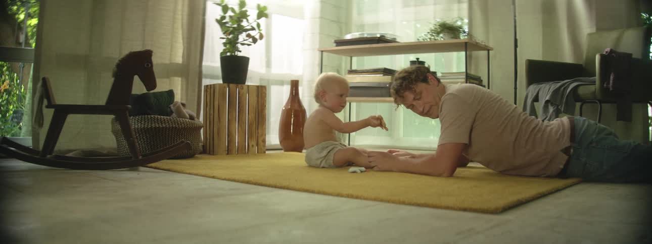 Father laying on floor playing with baby son on the rug
